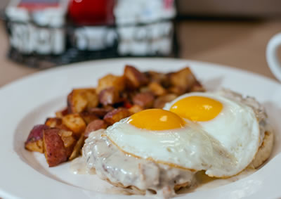 Country Breakfast: biscuit topped with two sausage patties, two eggs and sausage gravy, served with home fries