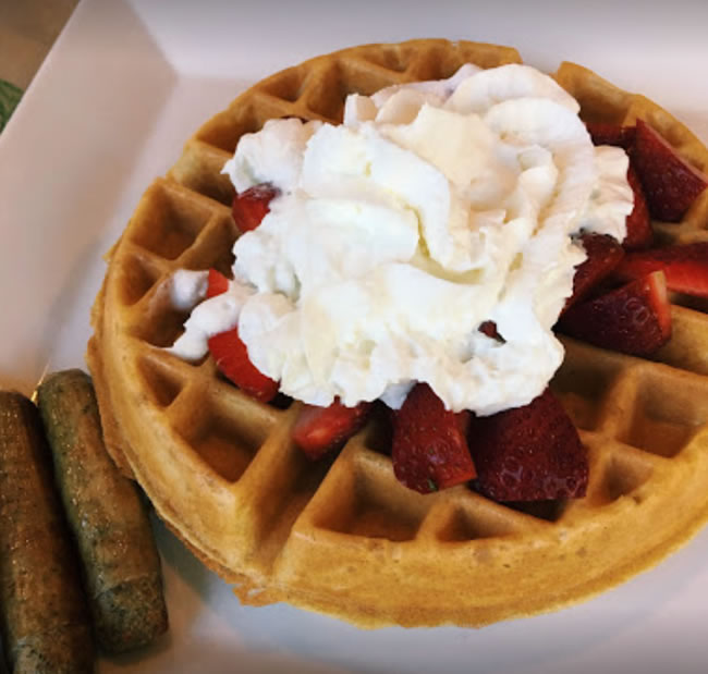 Belgian waffle topped with strawberries and whipped cream with two sausage links