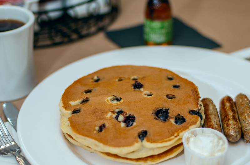 a plate of two blueberry pancakes, whipped butter and three sausage links