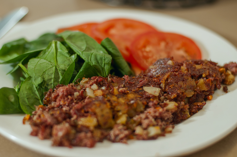 a plate of homemade corned beef hash with leafy greens and sliced tomatoes