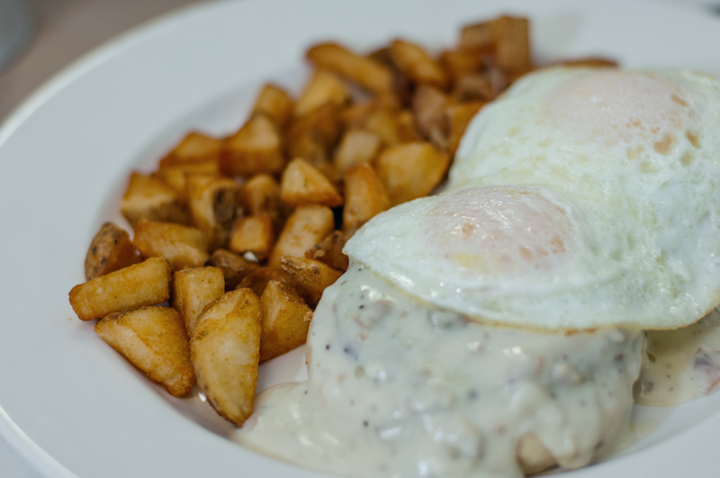 a plate of biscuit, sausage patties and gravy, sunny-side up eggs with home fries