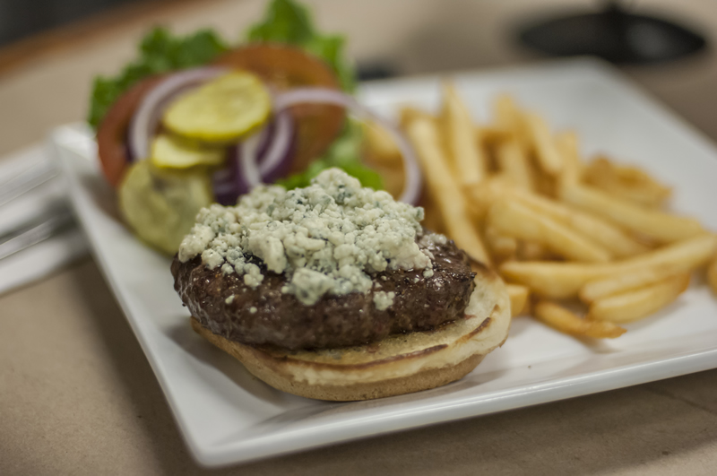 homemade hamburger topped with crumbled blue cheese, side of lettuce, tomato, pickle, onions and french fries