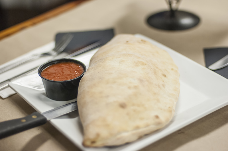 a plated calzone filled with filled with ricotta, mozzarella and cheddar cheese and side of marinara