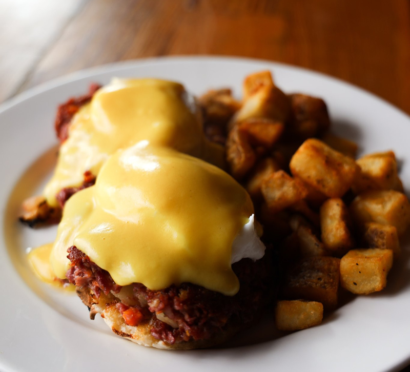 Traditional Eggs Benedict: English muffin topped with poached eggs, corned beef hash and hollandaise with home fries