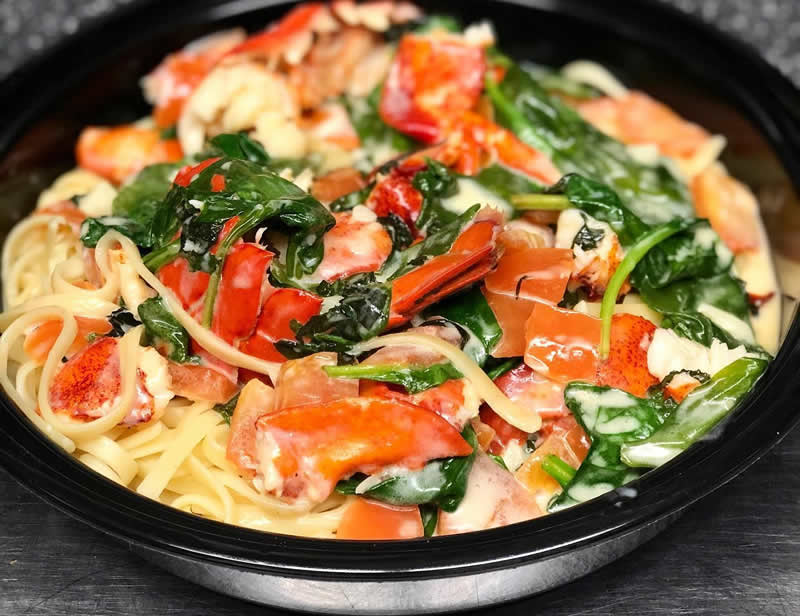 Plate of Lobster Florentine, sautéed lobster meat and tail in a rich cream sauce with tomatoes, fresh spinach and basil, tossed with linguini