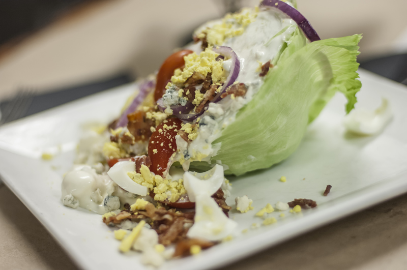 wedge salad with iceberg lettuce, pancetta, red onion, chopped egg and blue cheese dressing
